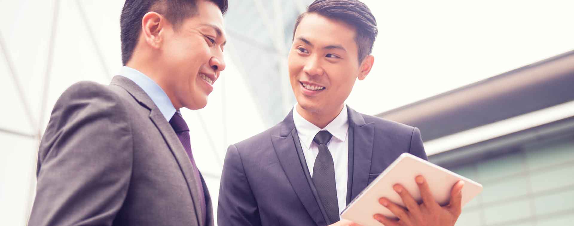 Smiling Chinese businessmen discussing something while one holds a tablet
