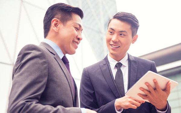 Smiling Chinese businessmen discussing something while one holds a tablet