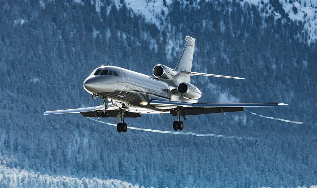 A metallic private jet flying over a snowy forest