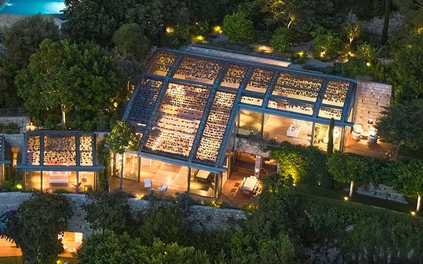 Aerial view of a lit-up modern villa surrounded by trees at nighttime