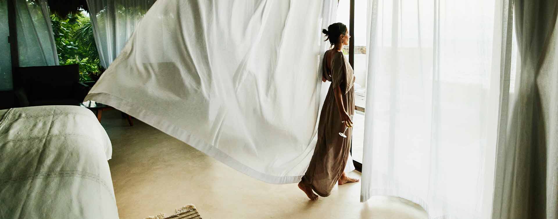 Woman standing in luxury hotel suite with curtains blowing in wind