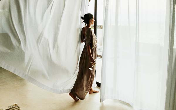 Woman standing in luxury hotel suite with curtains blowing in wind