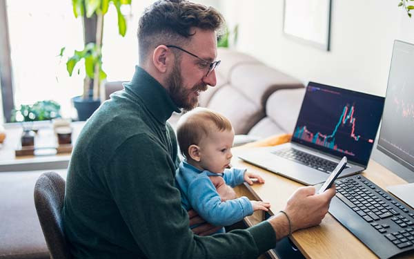 Man looking at trading app on his smart phone from home office with baby on lap