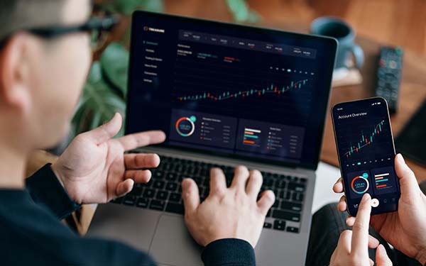 Young couple managing finance and investment online, analyzing stock market trades with mobile app on laptop and smartphone. Making financial plans. Banking and finance, investment, financial trading, crypto, mobile banking concept