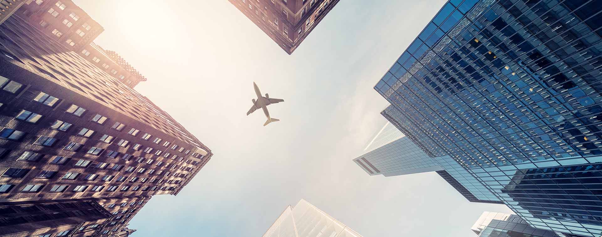 View of skyscrapers from the bottom up with a plane flying overhead.