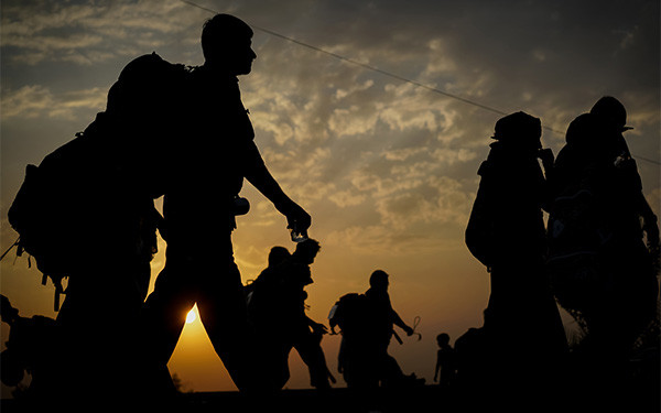 Group of immigrants carrying backpacks and walking at sunset