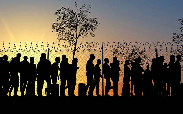 Line of people in silhouette by fence and barbed wire