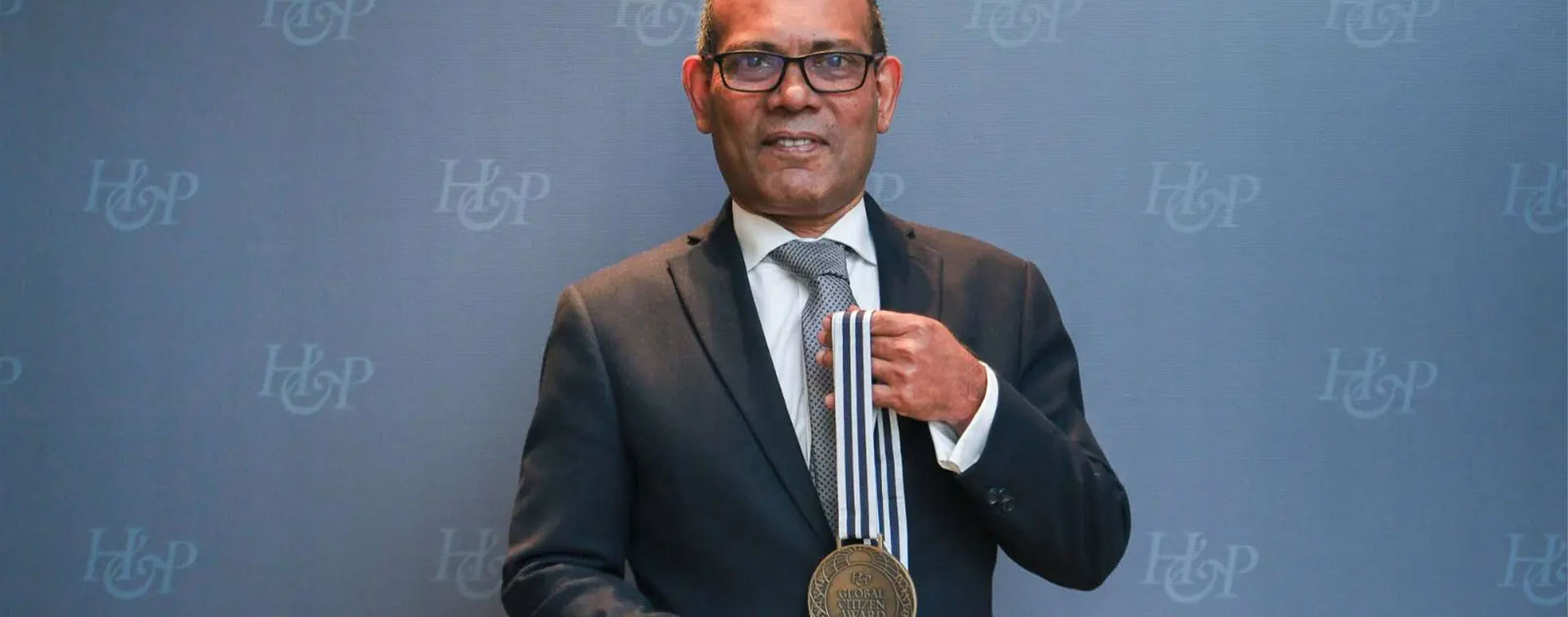 Global Citizen Award winner Mohamed Nasheed holding medal against an H&P-branded backdrop