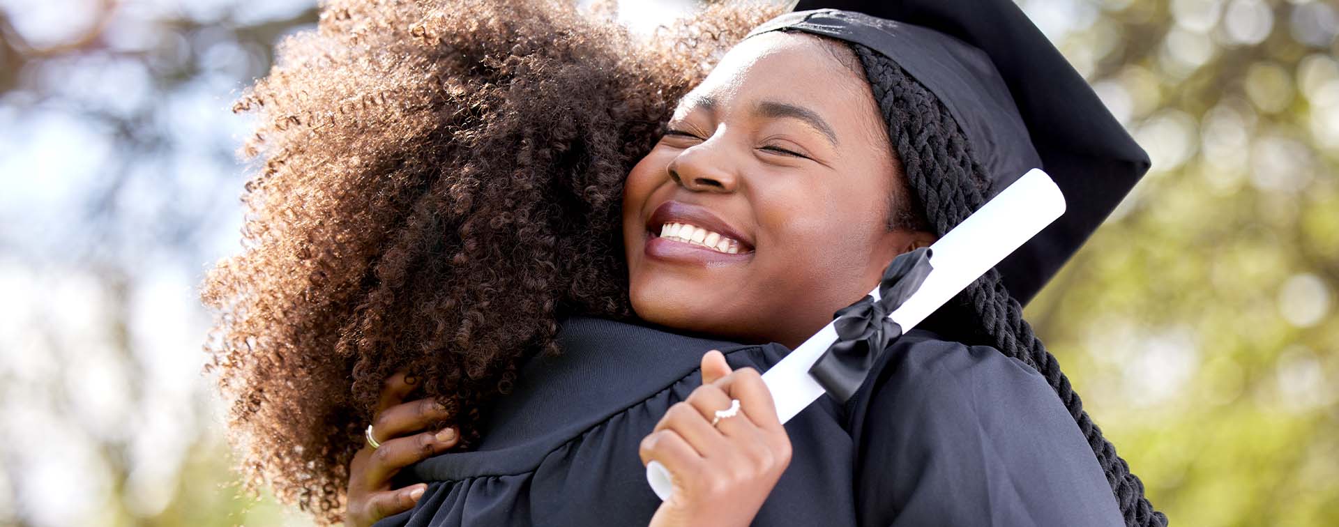 Happy graduates in cap and gown hugging outdoors