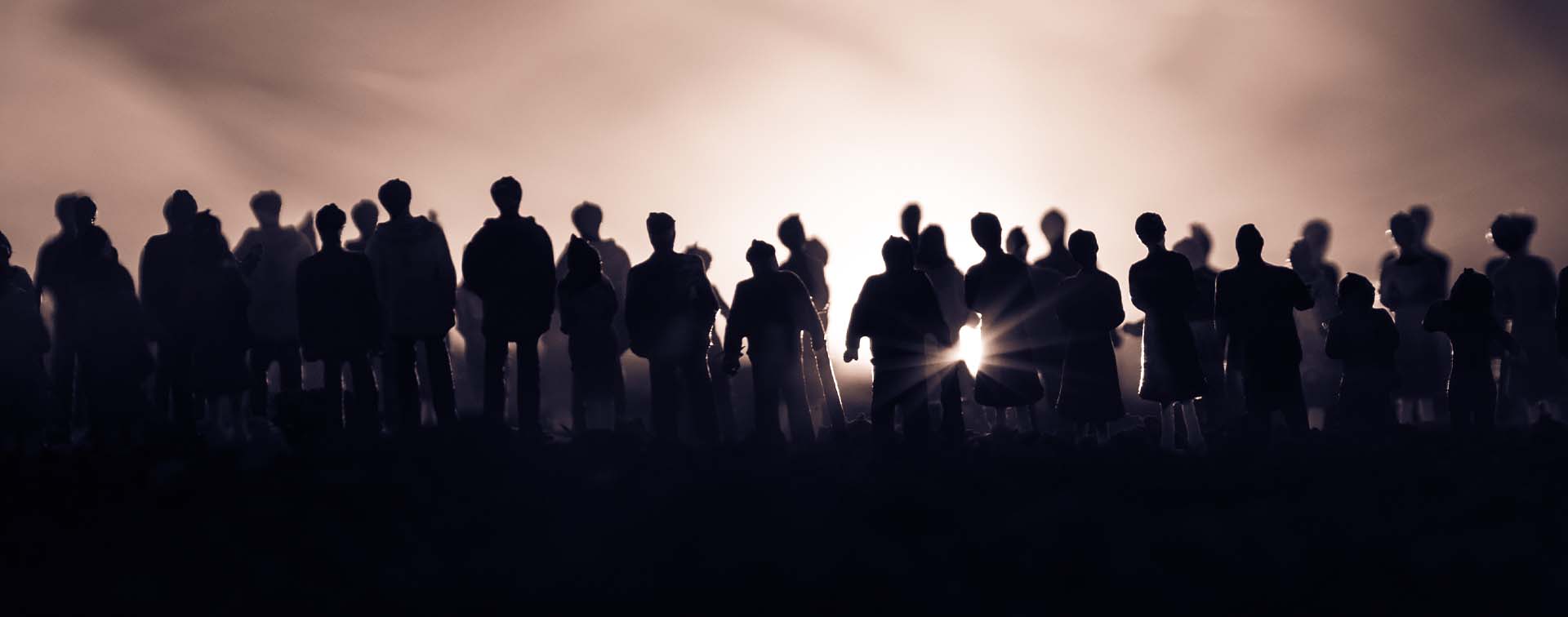 Silhouettes of a crowd against a bright horizon