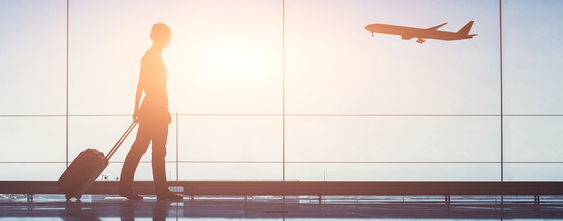 Traveler with a suitcase walking in an airport as a plane takes off