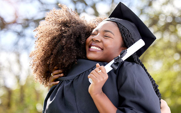 Happy graduates in cap and gown hugging outdoors