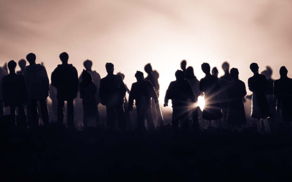 Silhouettes of a crowd against a bright horizon