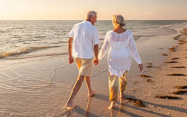 Happy Senior Old Retired Couple Walking Holding Hands on Beach at Sunset