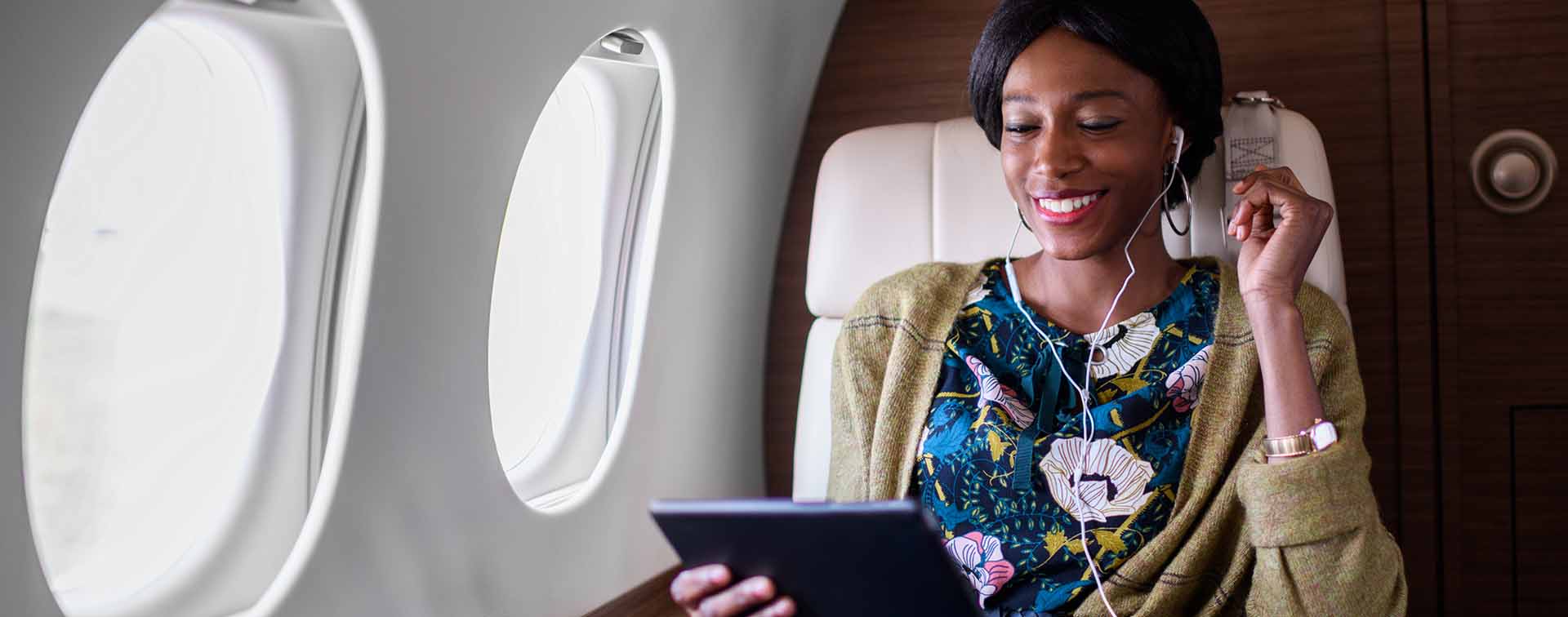 Black woman sitting inside private jet airplane and holding digital tablet