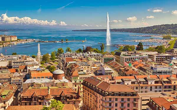 Geneva skyline cityscape, French-Swiss in Switzerland. Aerial view of Jet d'eau fountain, Lake Leman, bay and harbor from the bell tower of Saint-Pierre Cathedral. Sunny day blue sky
