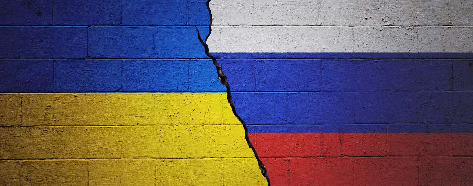Cracked brick wall painted with Ukraine flag on the one side and the Russian flag on the other side of the crack