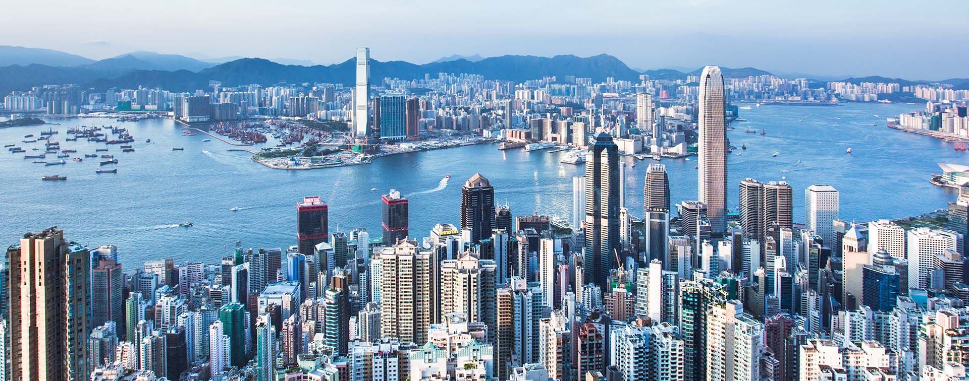 Aerial view of Hong Kong’s skyline, split by a large body of water, with a mountain range in the background