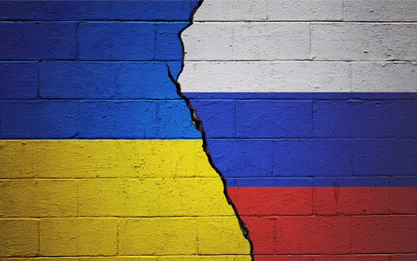 Cracked brick wall painted with Ukraine flag on the one side and the Russian flag on the other side of the crack