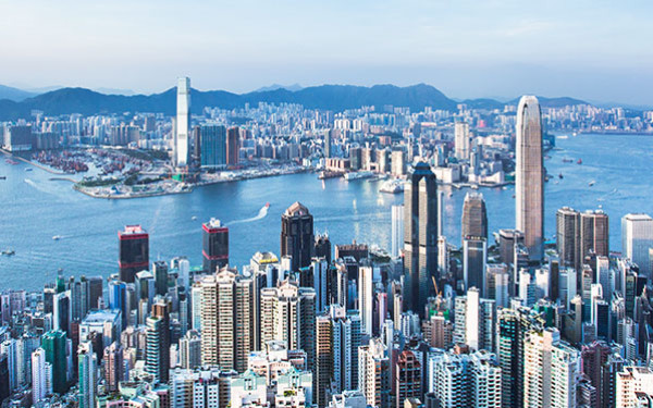 Aerial view of Hong Kong’s skyline, split by a large body of water, with a mountain range in the background