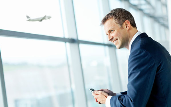 Smiling businessman looking to the left in front of large glass airport window as a plane takes off from the runway in the background
