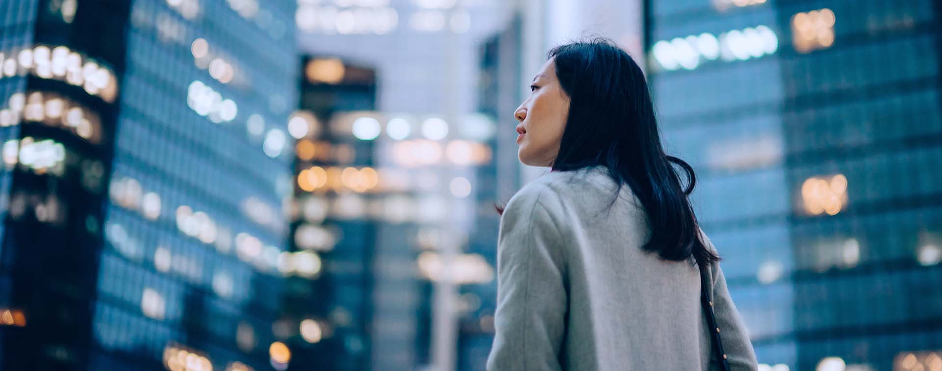 Side profile of a young Asian businesswoman standing among contemporary skyscrapers
