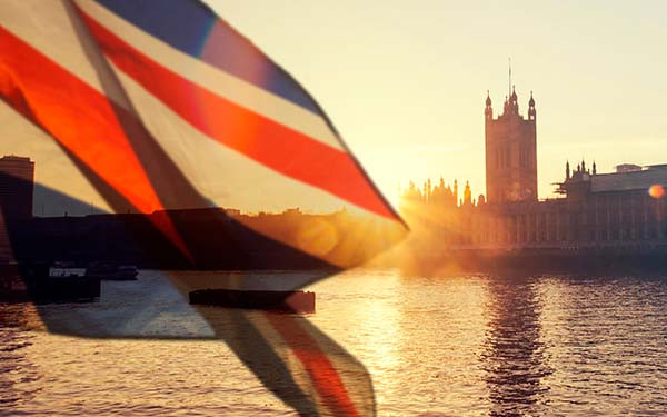 The UK flag flying in front of the London skyline at sunrise