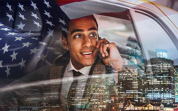 Businessman in a suit on mobile phone in cab with New York City buildings and US flag in the background