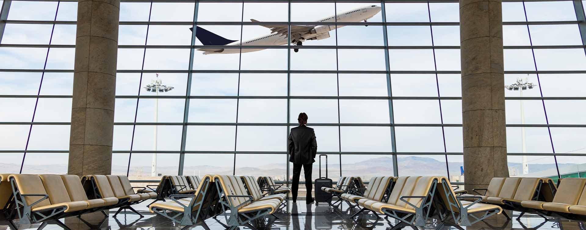 Businessman with luggage waiting in the airport looking out window as plane takes off