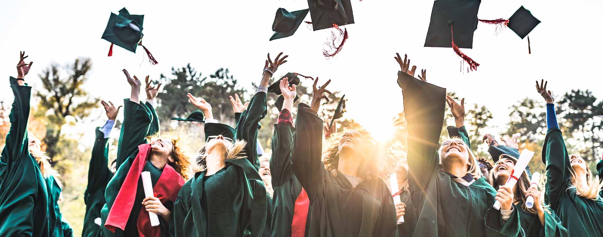 Large group of happy college students celebrating their graduation day outdoors while throwing their caps up in the air