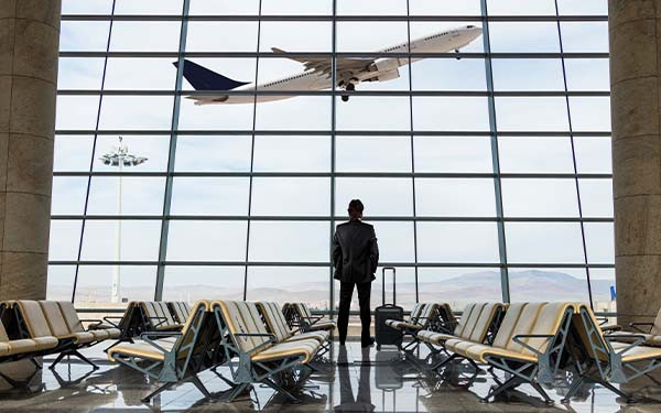 Businessman with luggage waiting in the airport looking out window as plane takes off
