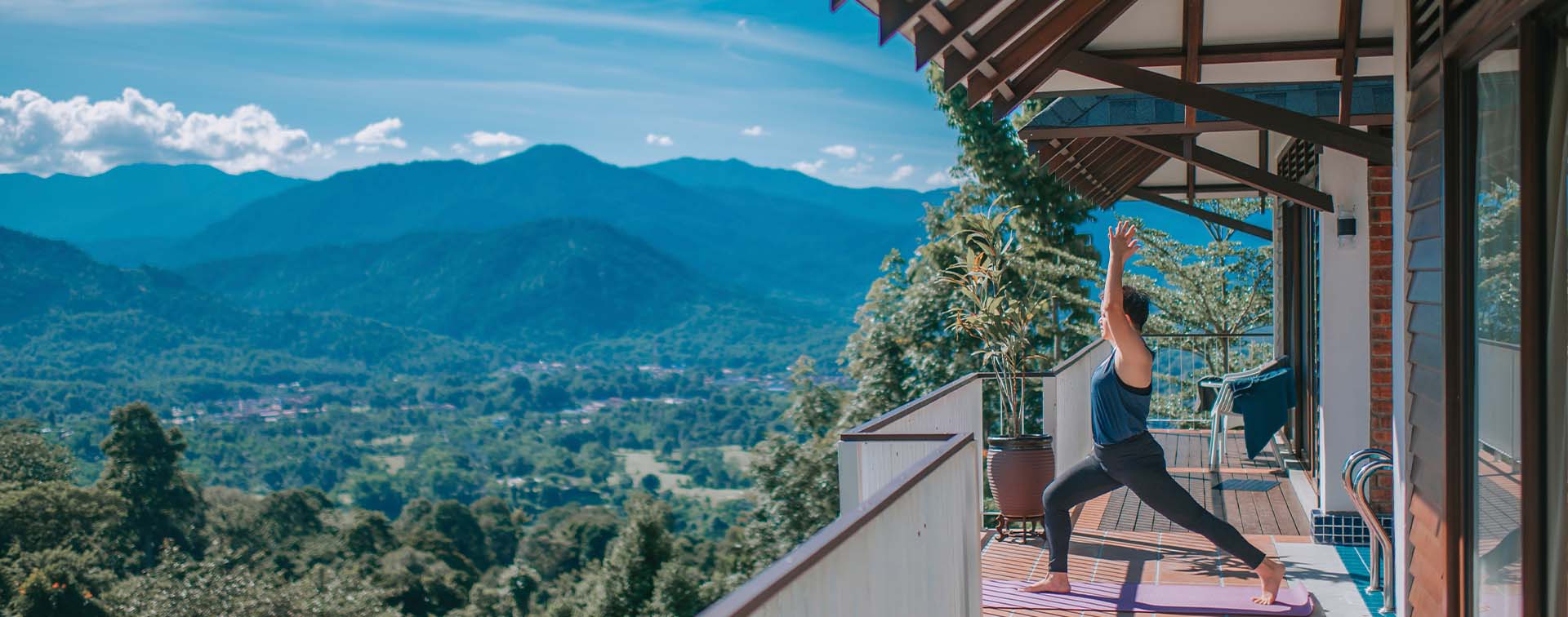 A woman practising yoga on a balcony overlooking a valley and mountains
